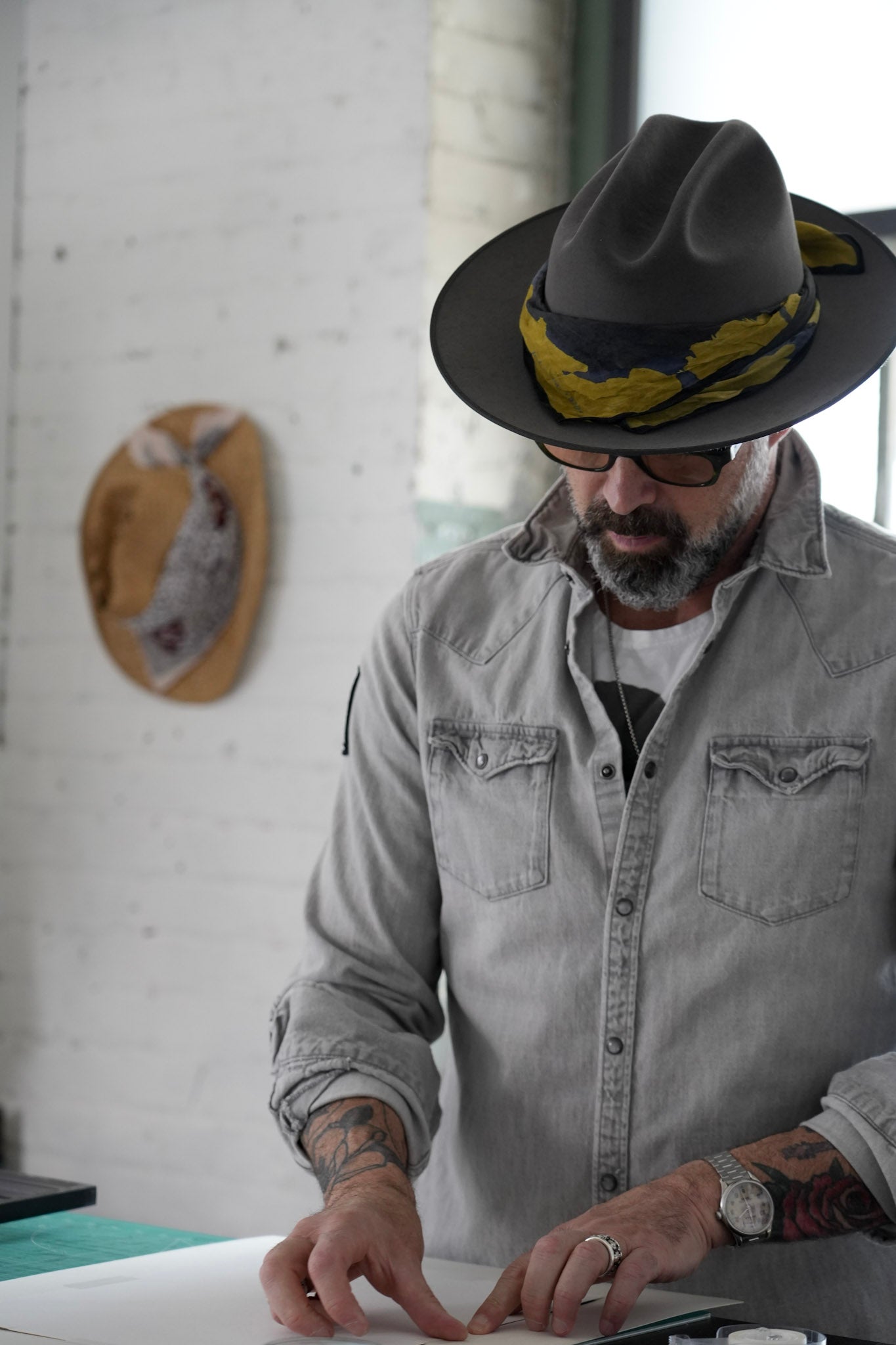 Man wearing a gray fedora and denim shirt, working on a project.