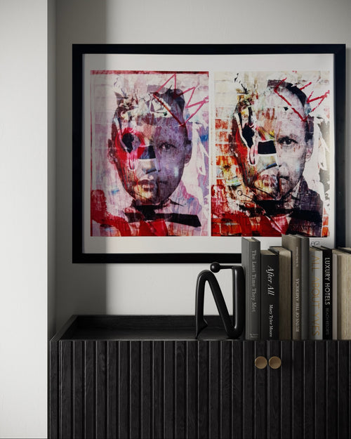 Framed abstract art piece on a wall above a shelf with books.