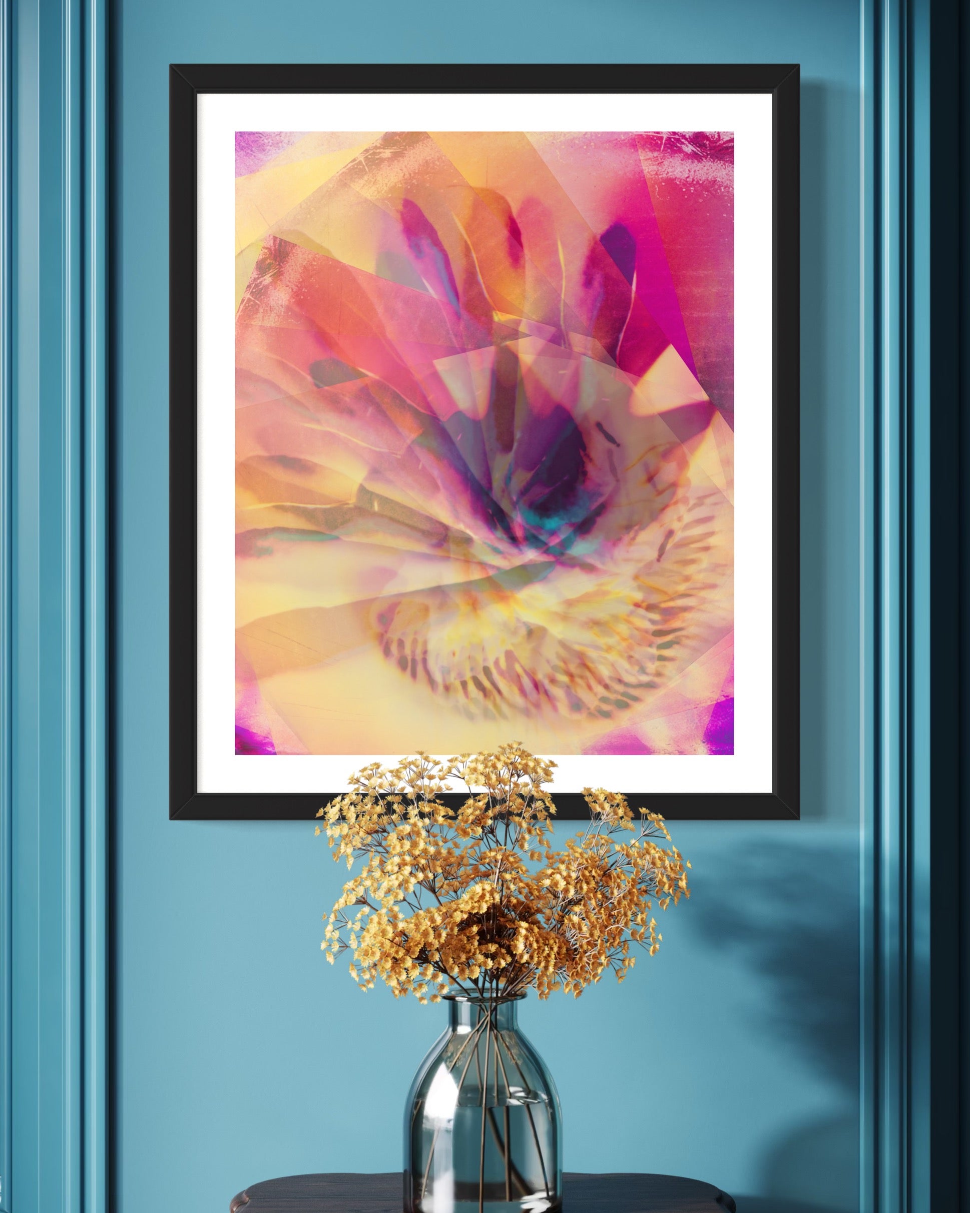 Framed abstract art on a blue wall with a vase of flowers below