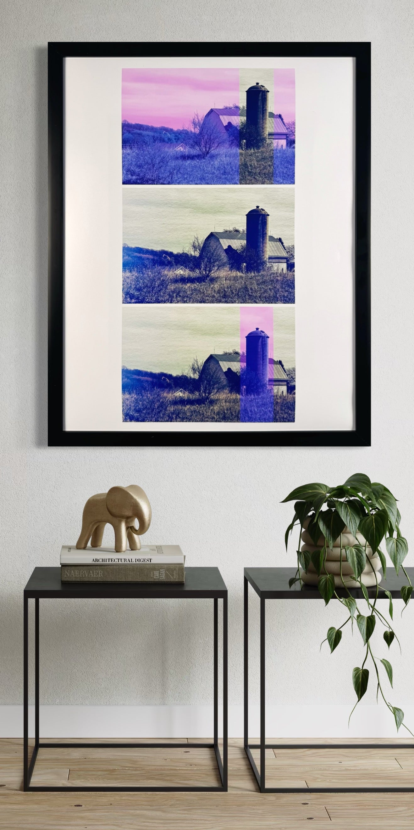 Framed artwork of a landscape with a silo on a wall above two side tables with decorative items.