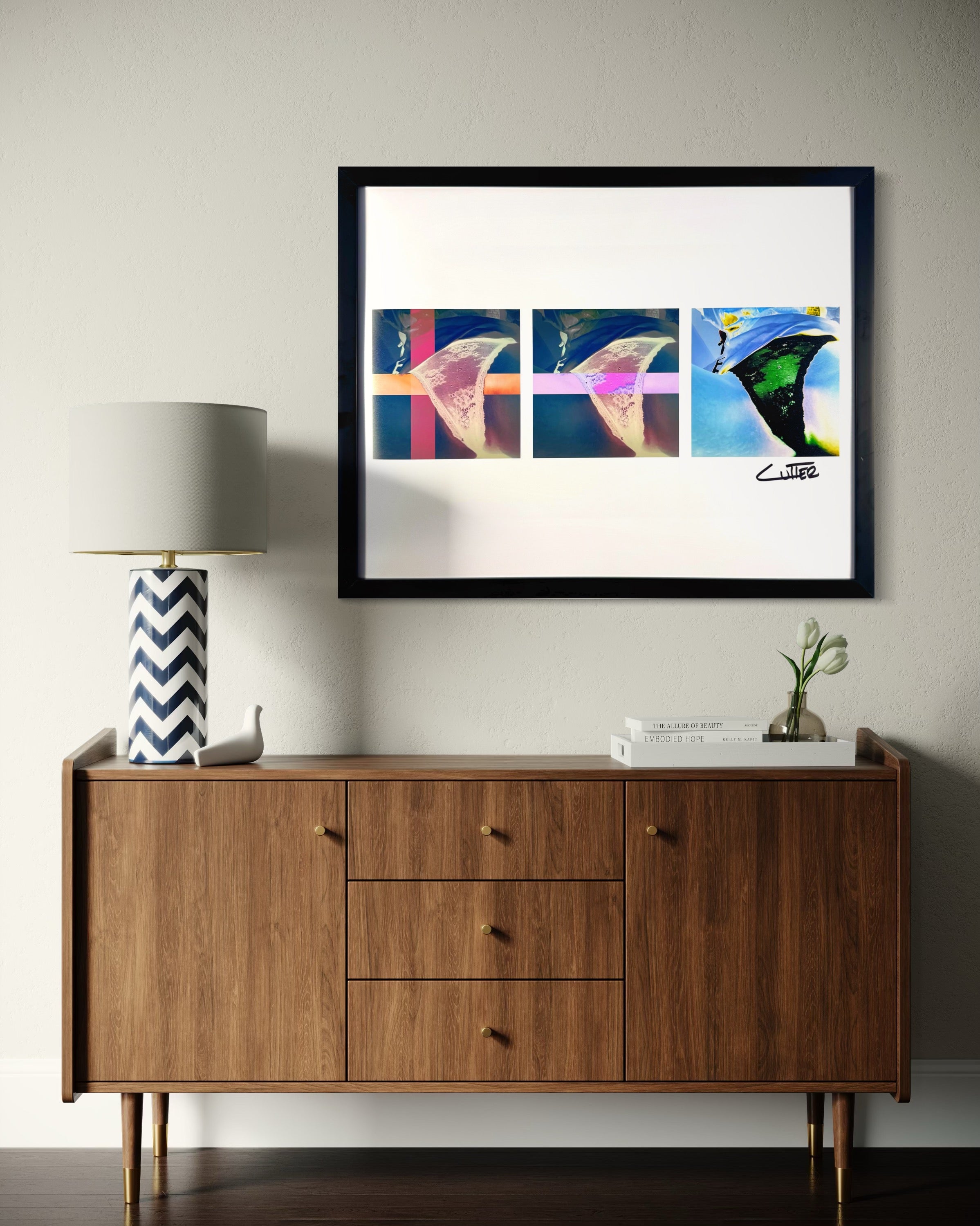 Framed abstract art above a wooden sideboard with a lamp and decorative items.